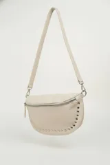 Cartera tipo riñonera o bandolera de cuero sintético negro con textura granulada, forma de media luna y detalles de tachas plateadas en el borde inferior. Cuenta con cierre metálico plateado y correa ajustable.