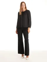 Blusa negra de gasa con cuello a la base fruncido, mangas largas amplias con puños elastizados y apliques de cinta con tachas en la parte delantera y antebrazos. Tiene una abertura central en la espalda con botón.