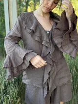 Camisa de lino azul marino con volados en cascada a lo largo del frente y en los puños de las mangas largas. Presenta un escote en V con un botón de nácar visible.