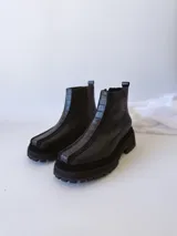 Botas negras de cuero con caña baja, cierre lateral con cremallera y suela track.