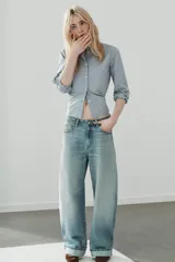 Jeans de tiro medio con cinco bolsillos, trabillas y cierre frontal con cremallera y botón metálico. Presenta un diseño baggy con piernas anchas, roturas decorativas y dobladillo vuelto en los bajos.