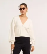 Cardigan corto de punto color blanco hueso, con escote en V, abotonado al frente y mangas largas abullonadas. Posee dos bolsillos delanteros tipo parche.