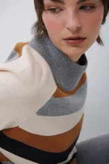 Polera de tejido de punto con diseño de rayas horizontales en tonos beige, marrón, gris y negro. Presenta cuello redondo y mangas largas con puños en contraste.