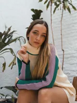 Buzo tejido de punto color crema con cuello alto y mangas largas con rayas horizontales en verde y lila.