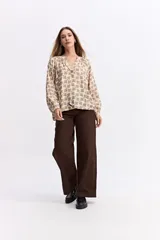 Blusa de corte relajado con estampado geométrico en tonos beige y negro. Presenta cuello en V con detalle de frunces, mangas largas abullonadas con puños elásticos y una caída fluida.