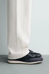 Zapatilla deportiva color verde militar, con parte superior de múltiples piezas que combinan piel y serraje. Presenta horma redonda y suela dentada en color crema con base marrón.