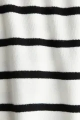 Buzo corto de punto suave, color blanco con rayas horizontales negras. Tiene cuello redondo y bajo recto.