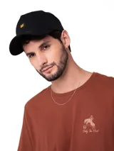 Gorro trucker negro de cinco paneles con malla en la parte trasera, visera curva y parche frontal redondo con el logo de Cat en amarillo.