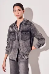 Camisa de denim celeste con cuello clásico, cierre frontal con botones a presión, dos bolsillos con solapa abotonada en el pecho y mangas largas con puños abotonados.