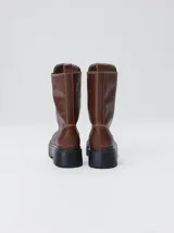 Botas de cuero color marrón de caña alta, con plataforma gruesa de goma y cierre metálico frontal con tirador. Presentan costuras a contratono y detalle de etiqueta de la marca en la lengüeta.