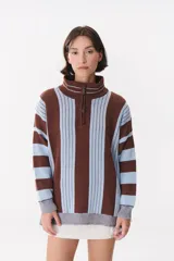 Buzo de tejido de punto con diseño de rayas verticales en tonos bordó y rojo. Presenta cuello alto con cierre frontal, mangas largas con coderas en contraste y detalles de costuras visibles.