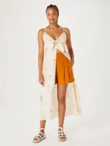 Musculosa tipo túnica de largo midi, con diseño estampado de flores en tonos claros y detalles en naranja. Presenta un escote en V con detalle de nudo frontal y breteles finos.