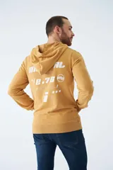 Buzo canguro color mostaza con capucha ajustable mediante cordones, bolsillo frontal tipo canguro y estampado gráfico en el pecho. Presenta puños y ruedo acanalados.