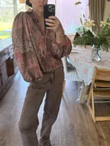Camisa de corte holgado con estampado estilo patchwork en tonos tierra, cuello clásico, cierre frontal con botones y mangas largas abullonadas con puños elásticos.