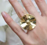 Anillo dorado con forma de flor con centro abultado y superficie texturizada.
