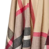 Poncho abierto de tejido de punto con diseño de cuadros escoceses en tonos beige, negro, blanco y detalles en rojo. Presenta terminaciones con flecos en el ruedo.