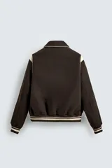 Cazadora estilo varsity de corte cropped, confeccionada en tejido de lana marrón con mangas en contraste color crema. Presenta cuello solapa, cierre frontal con botones a presión, bolsillos laterales de vivo y acabados en rib a rayas en puños y cintura.