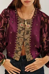 Saco de estilo bohemio confeccionado en terciopelo color violeta, con mangas largas abullonadas de tela fluida estampada. Presenta un panel central bordado con detalles ornamentales y cierre frontal.