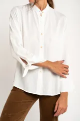 Camisa blanca de manga larga con cuello mao y cierre frontal con botones. Las mangas tienen nudos decorativos en los puños.