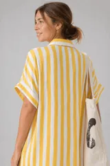 Vestido camisero de corte holgado y silueta relajada, con cuello clásico, cierre frontal de botones y mangas cortas con dobladillo. Presenta un estampado de cuadros irregulares en color bordó sobre fondo blanco.