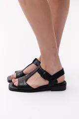 Sandalias negras de cuero con diseño de tiras en forma de T y hebilla lateral.
