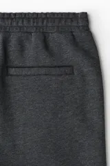 Pantalón tipo jogger de punto en tono gris oscuro, con cintura elástica y cordón ajustable. Presenta un pliegue cosido en el frente de cada pierna, bolsillos laterales y un bolsillo insertado trasero.