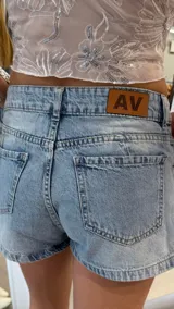 Short pollera de jean de tiro bajo en color celeste claro, con diseño cruzado que simula una falda en la parte delantera y bolsillos clásicos.