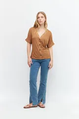 Remera marrón de tejido liso, con escote en V, mangas cortas y cierre frontal con botones.