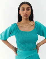 Top corto de color turquesa con cuerpo fruncido tipo nido de abeja, escote cuadrado y mangas abullonadas.
