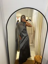 Vestido largo de fiesta color verde, confeccionado en tafeta con brillo y gasa. Presenta un diseño de un solo hombro con una capa de seda liviana integrada que permite diversas formas de uso, aportando movimiento y elegancia.