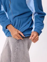 Campera de polar marca Rusty, color azul con paneles laterales en celeste claro. Presenta cierre frontal completo, cuello alto y logo de la marca bordado en el pecho.