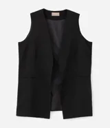 Chaleco sastre de corte alargado, color negro, con escote en V profundo y diseño sin mangas. Presenta un estilo minimalista con bolsillos laterales simulados y ajuste entallado en la espalda.