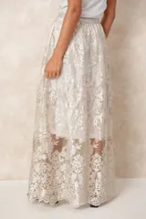 Pollera larga de tul con bordados florales en tono crema. Posee un forro interno opaco que llega hasta la rodilla, creando un efecto de transparencia en la parte inferior.