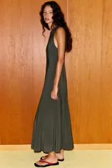 Vestido midi color verde oscuro, confeccionado en tejido fluido. Presenta cuello redondo, manga sisa y bajo con línea evasé y pliegues. Tiene cierre lateral con cremallera oculta y cierre en la espalda con abertura y botón.