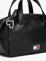 Cartera de mano tipo bowling color negro, confeccionada en poliuretano. Presenta doble asa superior, correa ajustable extraíble y el logo metálico de Tommy Jeans en la parte frontal.