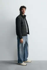 Cazadora acolchada de cuello subido, color negro, con mangas largas de tejido elástico. Incluye bolsillos en la cadera, un bolsillo interior y bajo con elástico. Cierre frontal de cremallera.