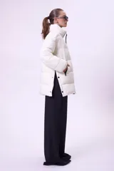 Campera puffer de corte oversize y largo medio, color blanco, con cuello alto, cierre frontal y aberturas laterales con botones a presión.