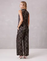 Conjunto de dos piezas compuesto por una blusa sin mangas con cuello solapa y escote en V con botones frontales, y un pantalón de tiro alto con pierna ancha y bolsillos laterales. Ambas prendas están confeccionadas en satén con un estampado floral sobre fondo oscuro.