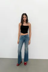 Top crop corsetero negro de popelín con escote recto, tirantes finos ajustables con lazada y bajo acabado con volante. Tiene forro interior a tono y cierre de cremallera en la espalda.