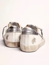 Zapatillas urbanas Golden Goose modelo Super-Star, de cuero blanco con efecto desgastado. Presentan una estrella de animal print en el lateral, talón plateado y cordones grises con inscripciones.