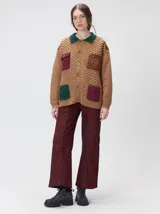 Campera tejida de punto grueso en color beige, con cuello en contraste color verde. Presenta cierre frontal con botones, bolsillos delanteros con apliques en nylon color marrón y bordado decorativo, y forro interno de nylon.