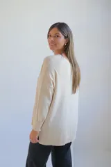 Sweater de punto color crudo, con escote en V, manga larga y diseño holgado con costura central vertical.