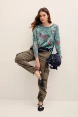 Sweater de punto con estampado floral en tonos rosados sobre base verde, cuello redondo y mangas largas.
