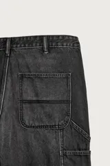 Pantalón jeans relaxed fit de mezclilla azul oscuro, con estilo carpintero que incluye bolsillos laterales y presillas de herramientas. Cuenta con costuras pespuntadas en contraste y cierre frontal con botón y cremallera.