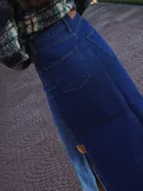 Pollera larga de denim azul de tiro medio, con diseño de corte evasé y terminación desmechada en el ruedo. Cuenta con abertura lateral y detalle de parche de cuero.