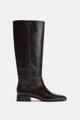 Bota de piel color marrón oscuro, de caña alta, con detalle de pespuntes en el cuerpo, tacón medio en bloque y punta cuadrada.