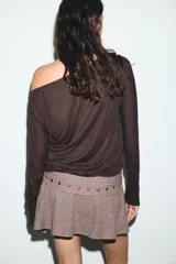 Camiseta de cuello barco y manga larga tipo murciélago, confeccionada en tejido de punto gris melange. Presenta detalle de tachas metálicas a lo largo de los hombros y las mangas.