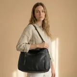 Bolso tipo morral y bandolera de eco-cuero negro, con cierre superior, bolsillos frontales con cierre y correa ajustable para el hombro.