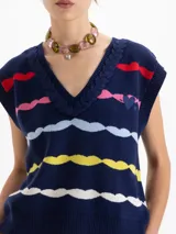 Chaleco de punto azul marino con escote en V y bordes trenzados. Presenta un patrón de ondas horizontales en colores rojo, rosa, azul claro, amarillo y blanco. Incluye un bordado tipo escudo en el frente.