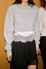 Sudadera crop de cuello redondo y manga larga con puños elásticos. Presenta un diseño de doble capa con un top interior satinado y un bajo decorado con encaje a tono.